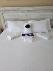 20230607_140334 - Mister Moppin - Mister Moppin Freshly made hotel-style bed with a wood headboard, folded white bath towels, and a navy welcome towel set staged after a post-clean inspection